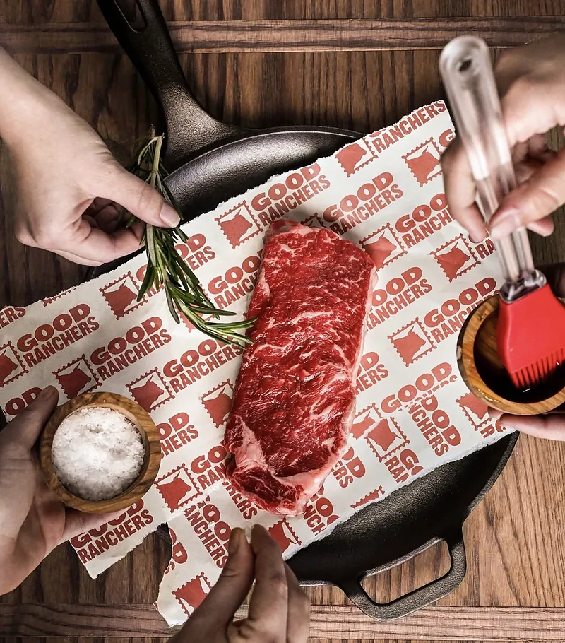 A raw steak on Good Ranchers branded paper with rosemary, salt and a basting brush
