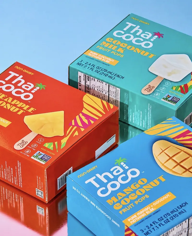 Three Thai Coco fruit pop boxes on a glossy blue surface
